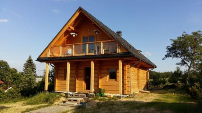 Gotowy drewniany dom z bali z balkonem i szklaną balustradą, widok z zewnątrz w słoneczny dzień.