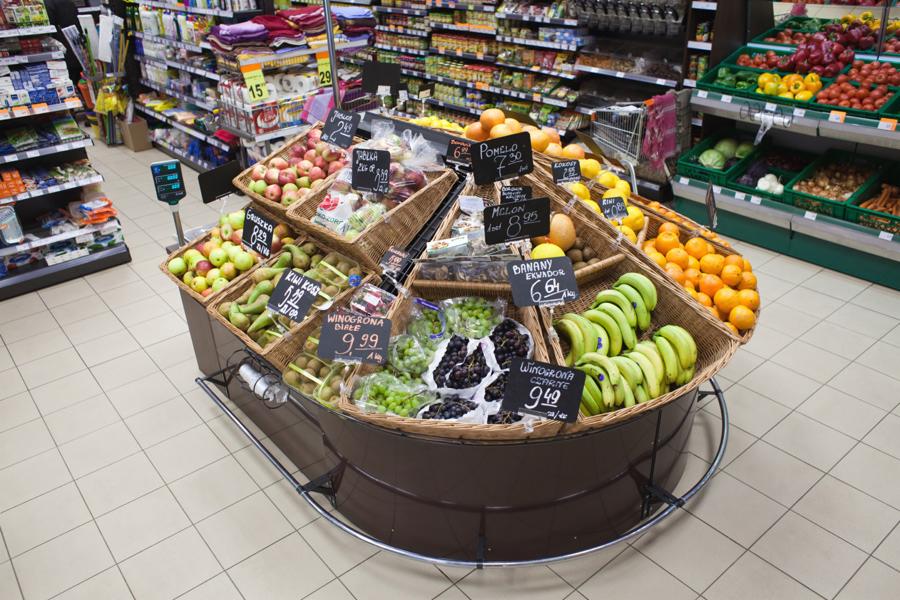 Ekspozycja różnorodnych owoców w koszach wiklinowych z cenami w supermarkecie, widok z góry.