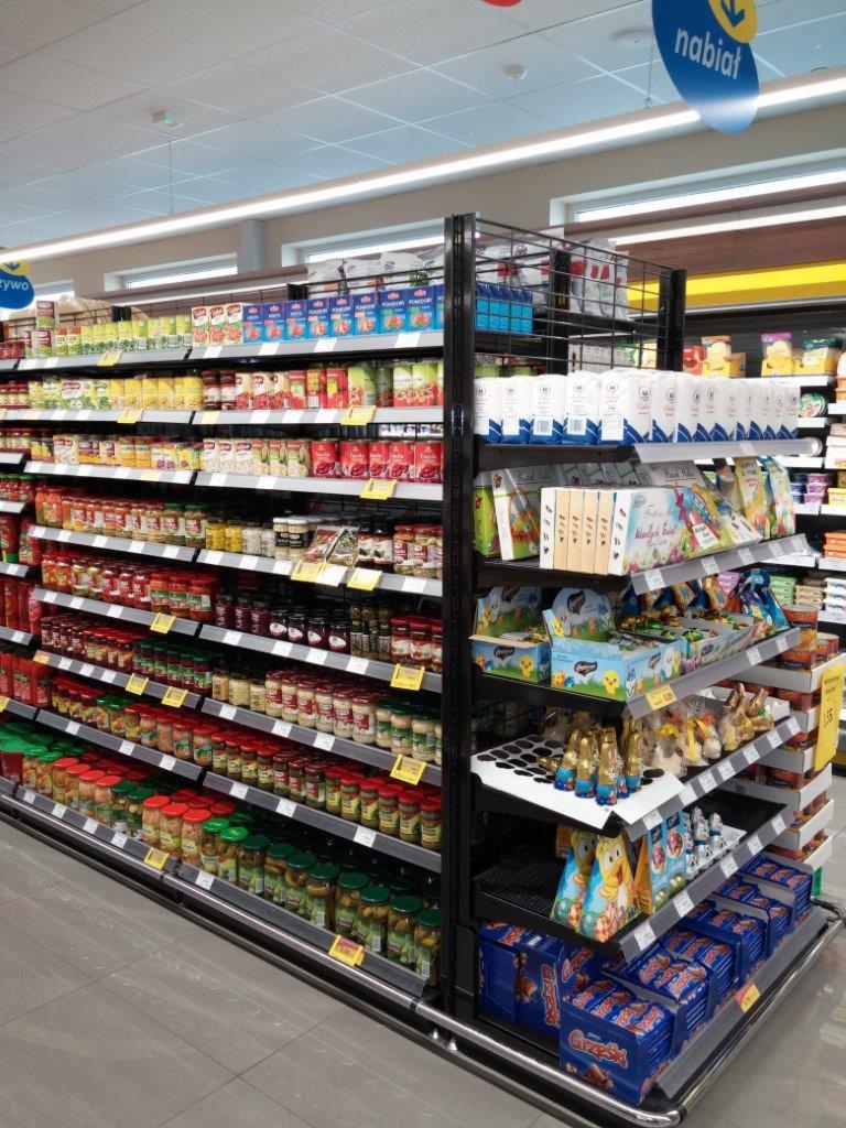 Półka sklepowa z metalową konstrukcją, wypełniona słoikami z przetworami, puszkami, pudełkami i innymi produktami spożywczymi w supermarkecie.