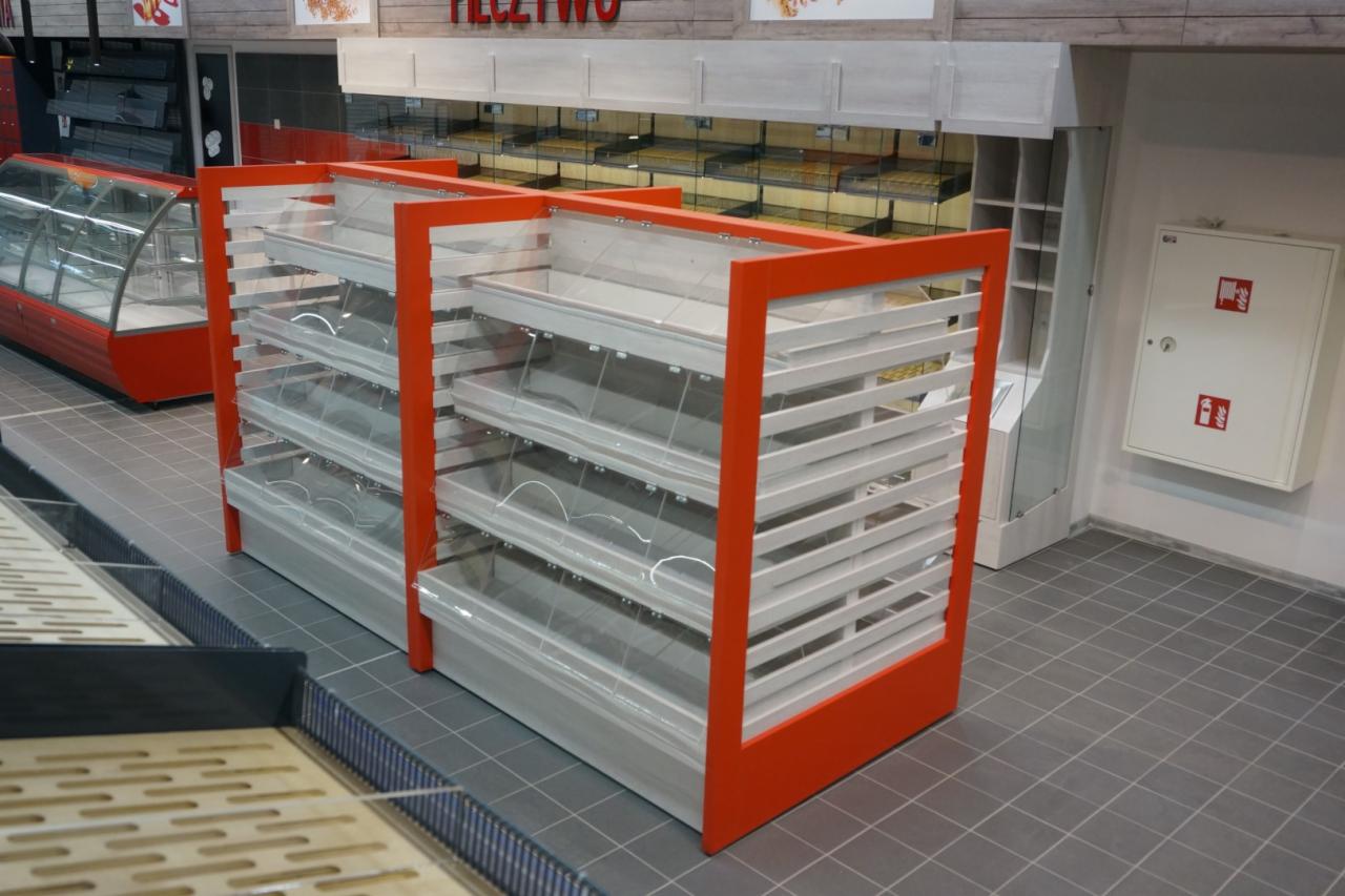 Puste, wielopoziomowe regały ekspozycyjne z pomarańczowymi ramami i przezroczystymi osłonami na półkach, ustawione na szarej podłodze w sklepie.