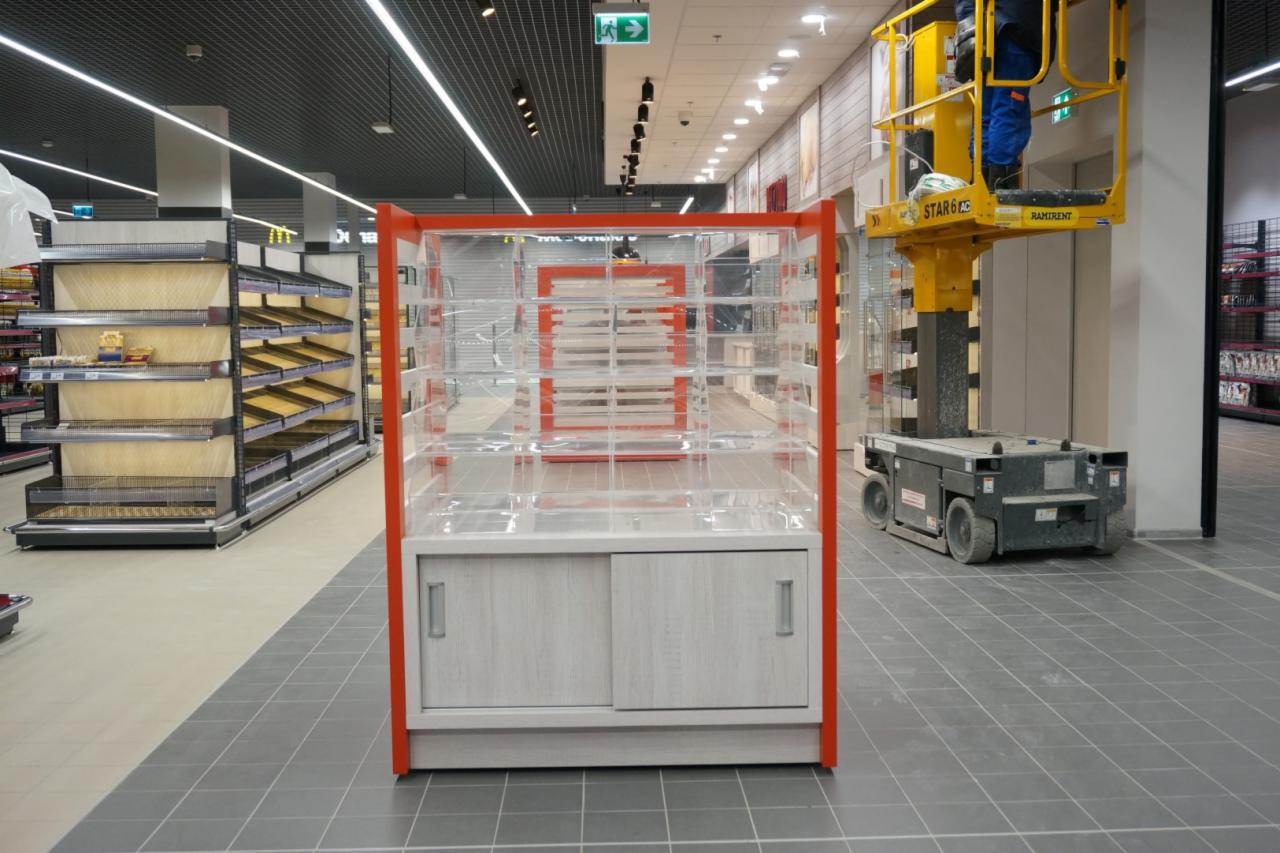 Montaż nowej, pustej witryny sklepowej z przeszkleniami i drewnopodobnymi drzwiczkami przesuwnymi w supermarkecie, widoczny podnośnik koszowy.