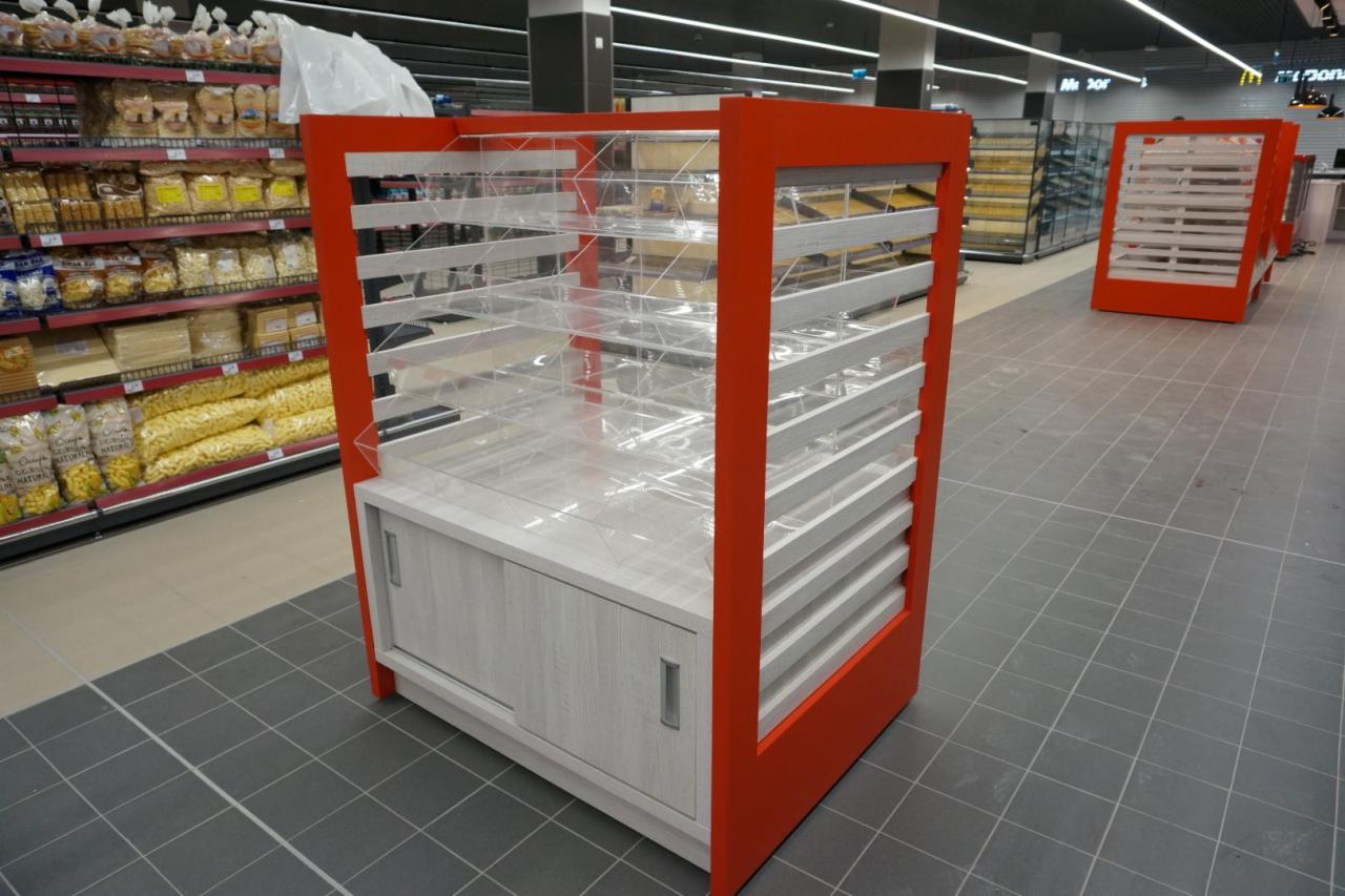 Półka ekspozycyjna z czerwonymi ramami i szarymi, przesuwnymi drzwiczkami w supermarkecie, z przezroczystymi półkami i białymi listwami, widok z perspektywy podłogi.