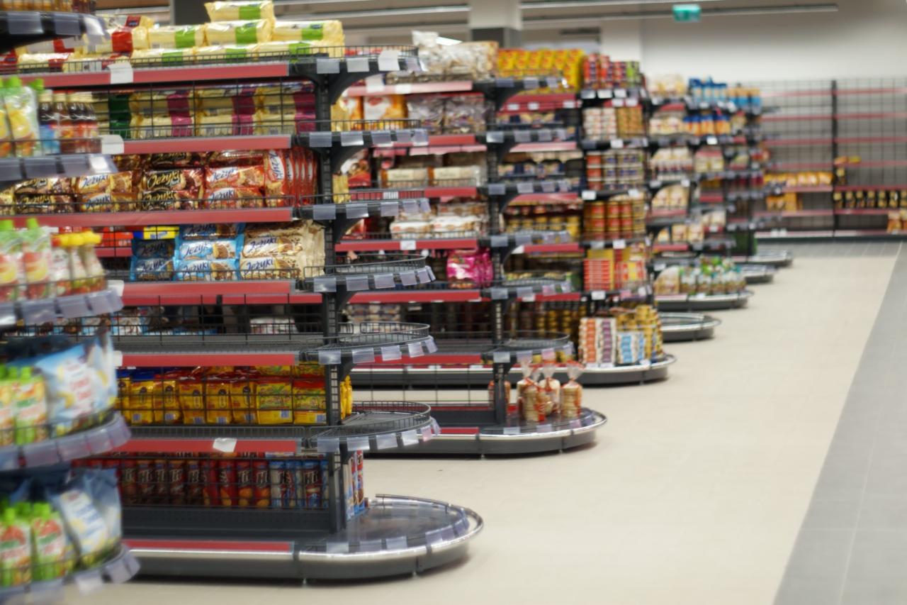 Półki sklepowe z produktami spożywczymi w Bytowie, widok z perspektywy klienta, zróżnicowany asortyment na metalowych regałach z czerwonymi akcentami.