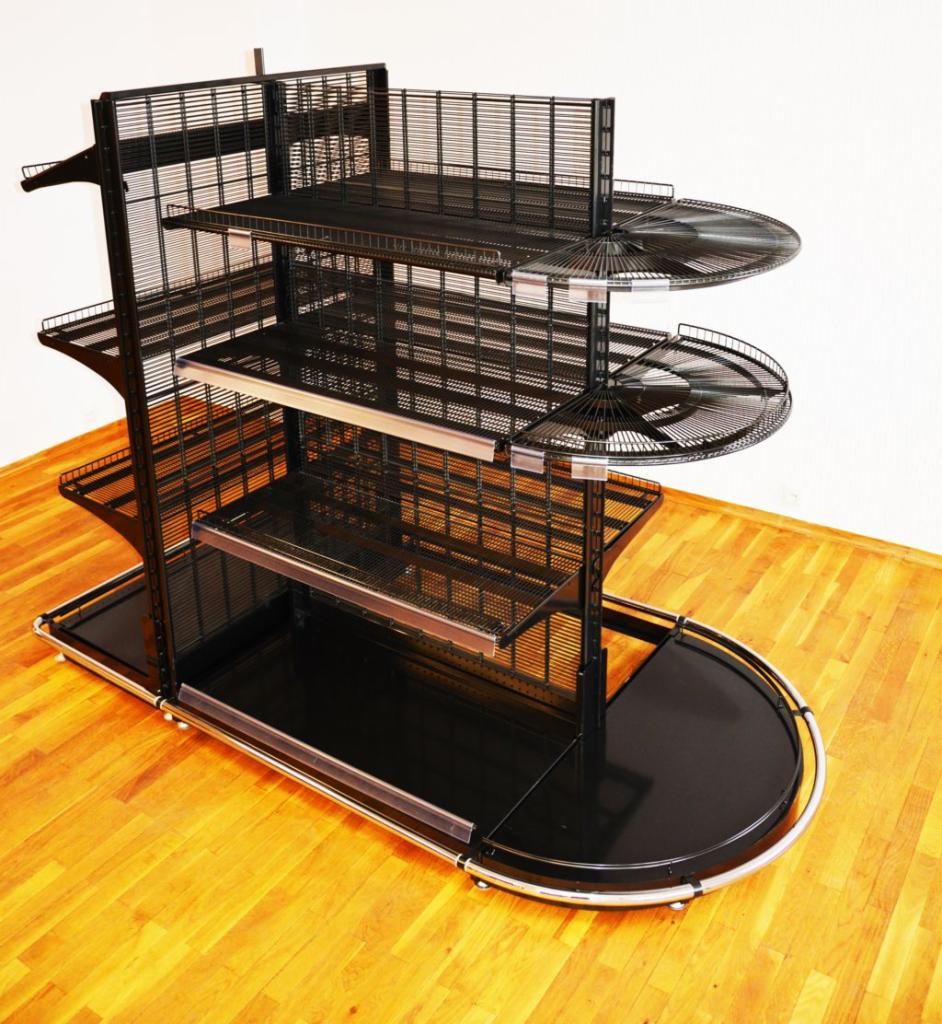 Czarny, metalowy regał sklepowy z półkami z siatki, o nietypowym kształcie, z zaokrągloną podstawą, stojący na parkiecie.