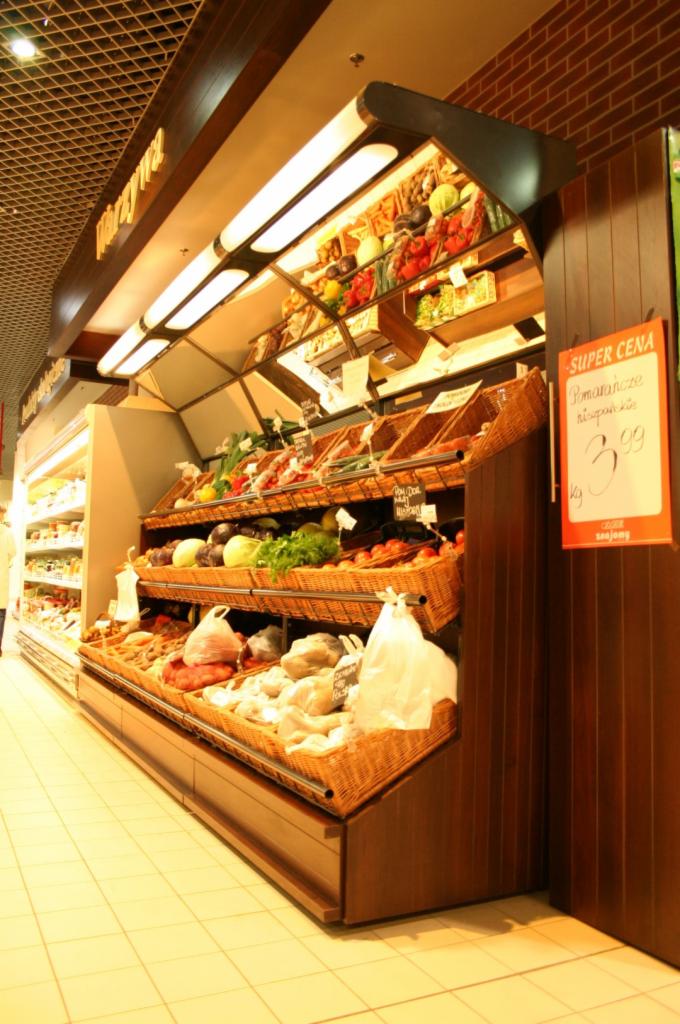 Wielopoziomowa ekspozycja warzyw i owoców w koszach wiklinowych podświetlona od góry w sklepie spożywczym.