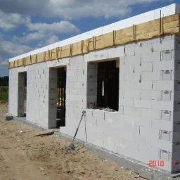 Surowy stan ścian budynku z betonu komórkowego, widoczne otwory okienne i drzwiowe, drewniane szalunki na górze, szpachelka oparta o ścianę, data 2010 7 20 w prawym dolnym rogu.