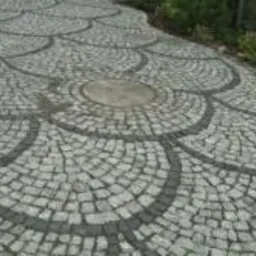 Ułożona z kostki granitowej ścieżka w ogrodzie, wzór wachlarzowy z ciemniejszymi obramowaniami, widok z góry.