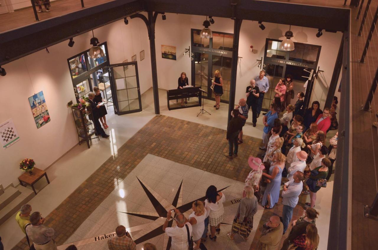 Wnętrze galerii z publicznością, pianinem i saksofonem podczas wydarzenia kulturalnego, widok z góry.