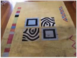 Żółty dywan z geometrycznymi wzorami, na którym leżą cztery kwadratowe kartki z różnymi motywami: pusty prostokąt, zebra, spirala, prostokąt z tekstem.