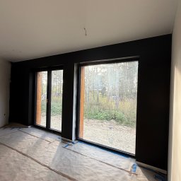 Luk Complex - Pokój po malowaniu na czarno, zabezpieczona podłoga folią i taśmą. Widoczne duże okna z widokiem na zewnątrz. Ściany pomalowane na jednolity kolor, sufit biały.