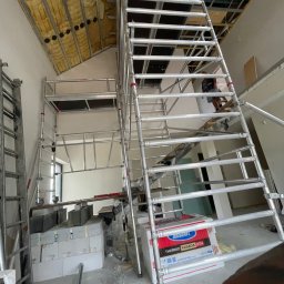 Luk Complex - Wnętrze w trakcie prac wykończeniowych: widoczny rusztowanie, ocieplenie poddasza wełną mineralną, białe ściany i materiały budowlane.