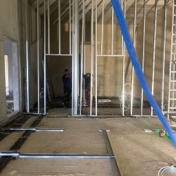 Luk Complex - Montaż metalowej konstrukcji ścian działowych w trakcie prac wykończeniowych w Pszczynie, widoczne przewody instalacji podłogowej i niebieski przewód wentylacyjny.