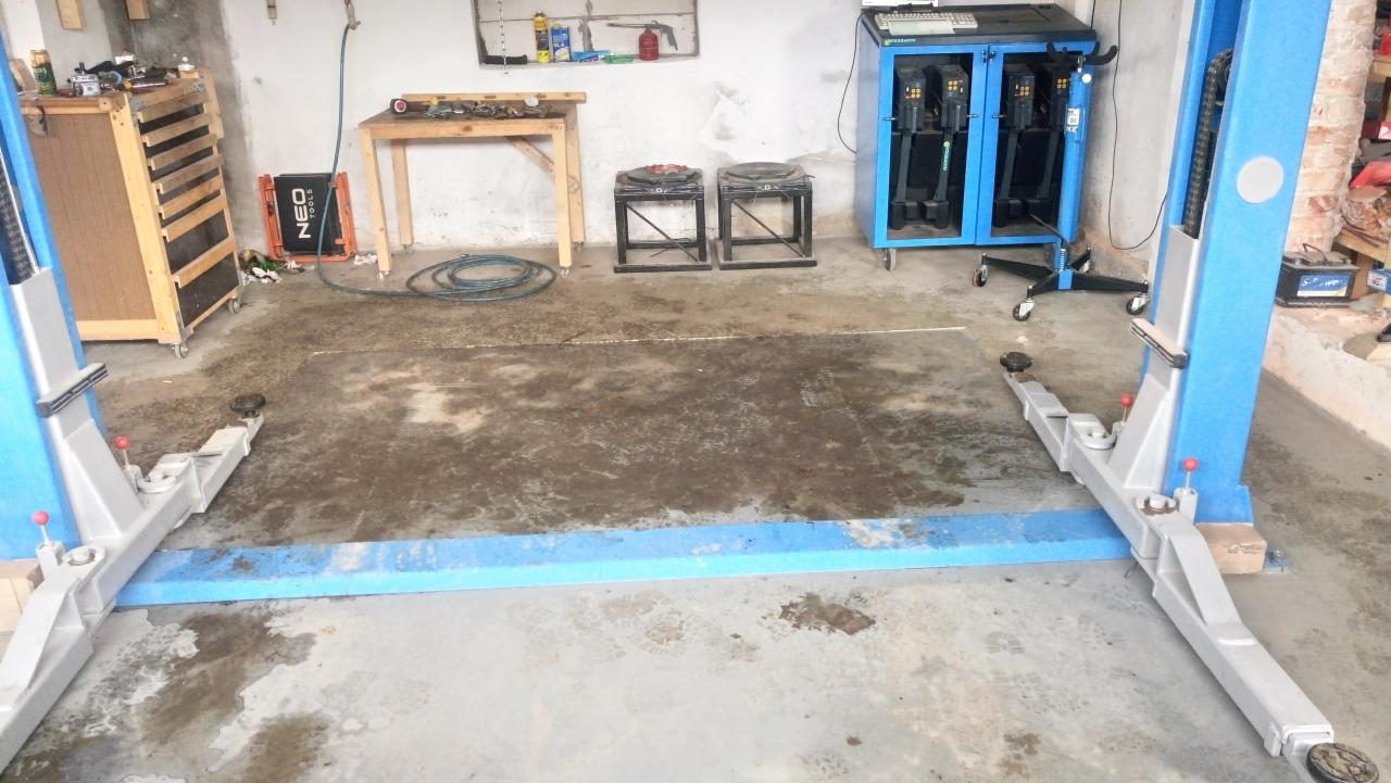 Dwukolumnowy podnośnik samochodowy w warsztacie, widoczne wyposażenie warsztatu, w tym narzędzia i stanowisko do diagnostyki kół.