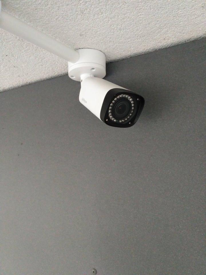 Biała kamera monitoringu Dahua zamontowana na suficie, widoczne diody IR i szara ściana w tle.