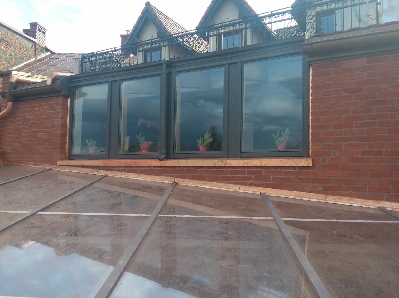 Ceglana dobudówka z dużymi oknami i przeszklonym dachem, widok z zewnątrz na fragment konstrukcji.