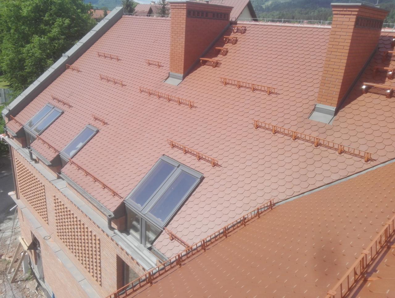 Czerwony dach z dachówki karpiówki na nowym, murowanym domu z cegły, z oknami dachowymi i ceglanymi kominami, widok z góry.