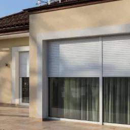 Elewacja domu z beżowego tynku z białymi oknami z opuszczonymi białymi roletami zewnętrznymi, widok z zewnątrz na okno z zasłoną.