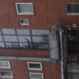 Montramex - Widok z góry na budynek z cegły z różnymi oknami, w tym oknami kratowymi i dużym oknem z podziałami, z widoczną rurą spustową i elementami wentylacji.