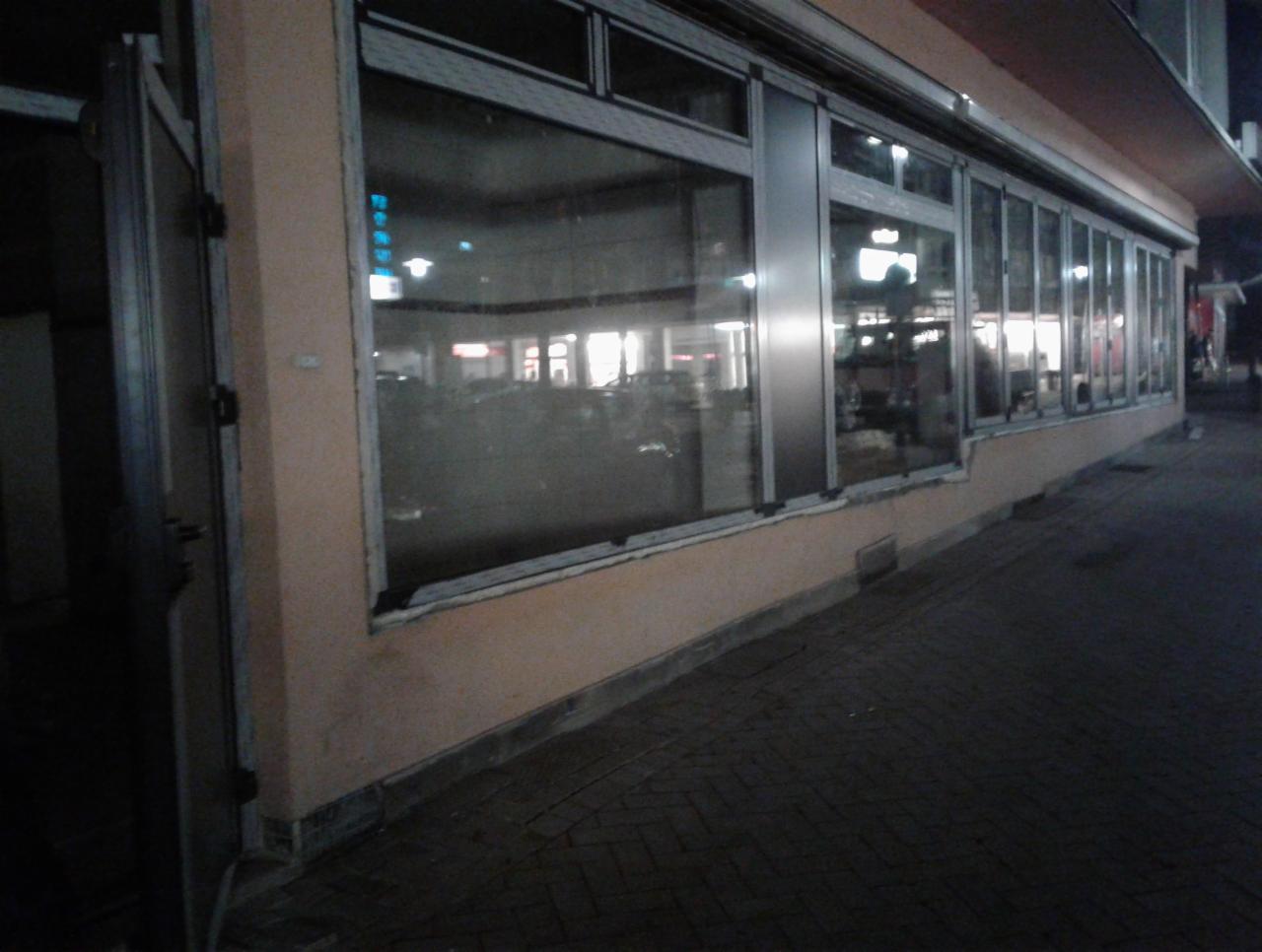 Zamknięte, przesuwne okna wystawowe i otwarte drzwi wejściowe do lokalu wieczorem, widok z zewnątrz.