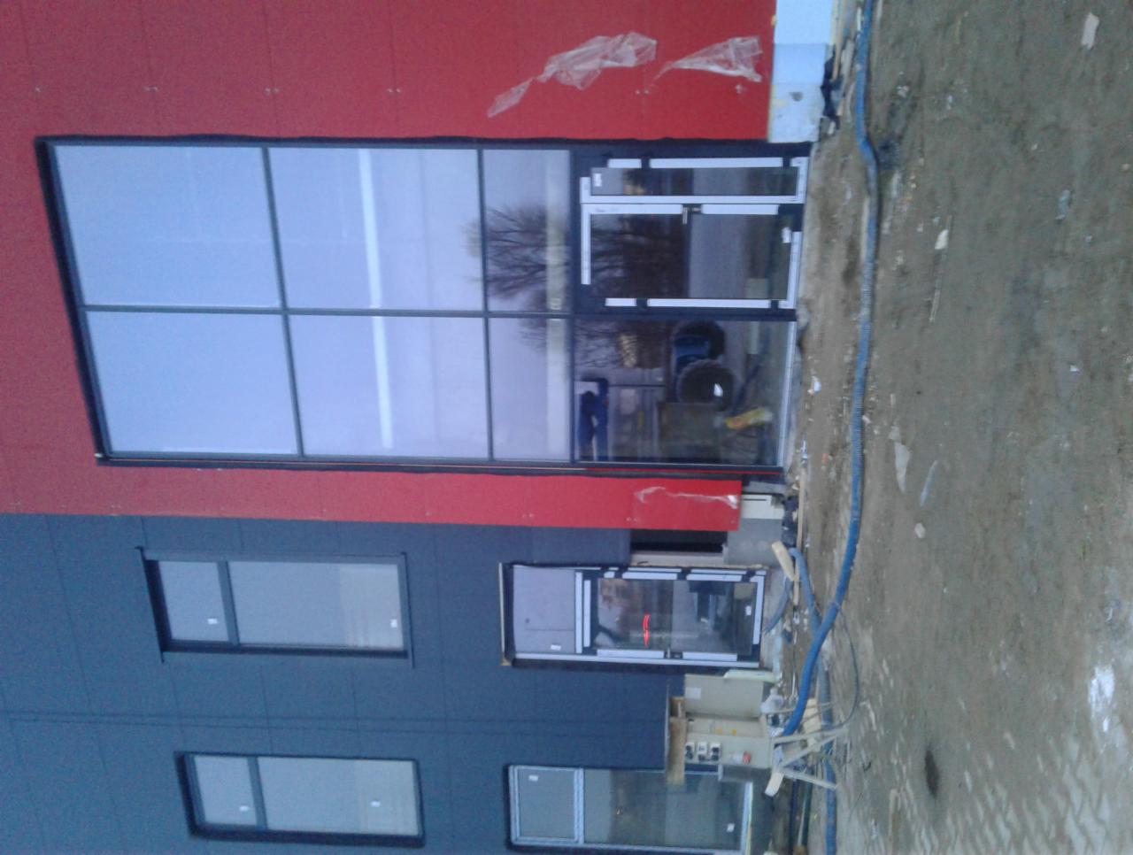 Nowoczesny budynek z zamontowanymi oknami i drzwiami aluminiowymi, widoczne ślady prac budowlanych na zewnątrz.