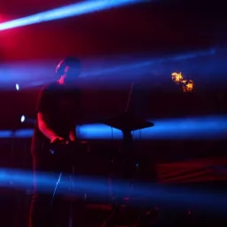 DJ w słuchawkach grający muzykę na konsoli DJ-skiej, oświetlony niebieskimi i czerwonymi światłami scenicznymi.