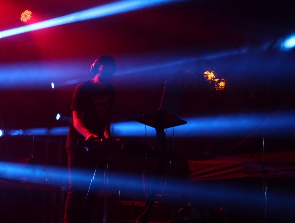 DJ w słuchawkach grający muzykę na konsoli DJ-skiej, oświetlony niebieskimi i czerwonymi światłami scenicznymi.