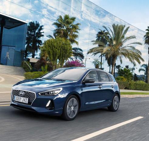 Niebieski Hyundai i30 na tle nowoczesnego budynku z palmami w Katowicach, dynamiczne ujęcie w ruchu.