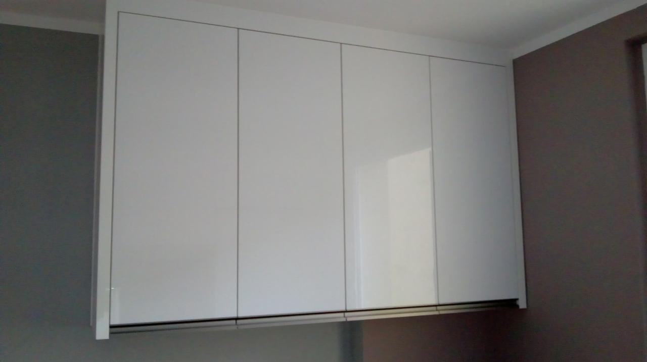 Białe szafki wiszące z czterema frontami, minimalistyczny design, widoczne na tle szarej i brązowej ściany.