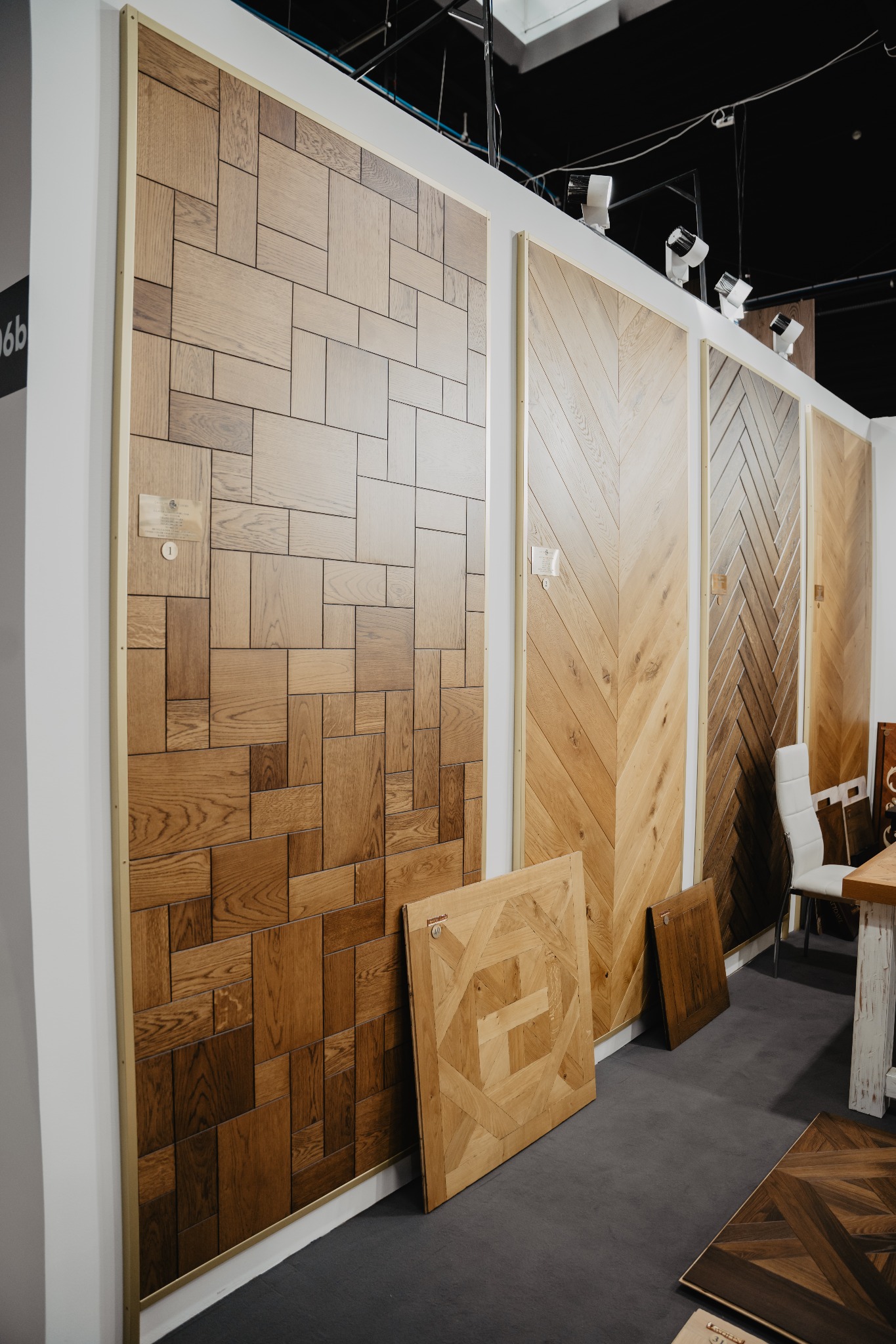 Ekspozycja różnych wzorów paneli podłogowych drewnianych na stoisku targowym, widoczne panele w geometryczne wzory oraz ułożone w jodełkę.