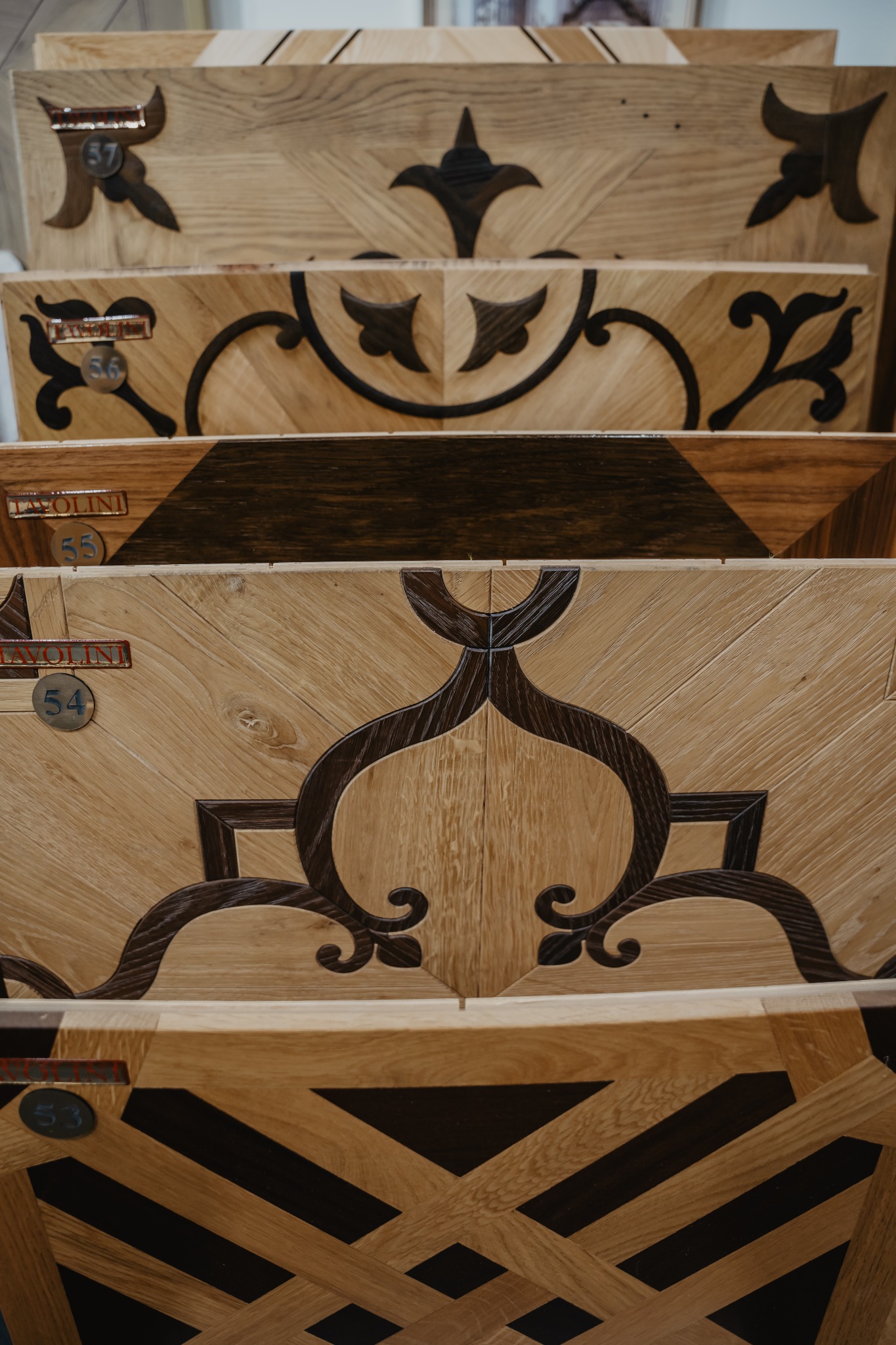 Różne wzory parkietu drewnianego w ekspozycji, z dekoracyjnymi intarsjami i oznaczeniami próbek.