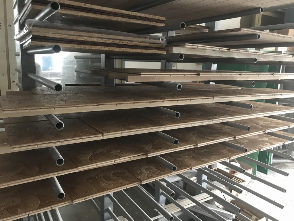 Panele drewniane z delikatnym wzorem, ułożone na metalowym regale z rurkami, prawdopodobnie w magazynie lub suszarni.