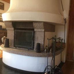 Kominki Szablinski - Tradycyjny, murowany portal z granitowym wykończeniem i czarnymi drzwiczkami, uzupełniony o zestaw akcesoriów kominkowych i dekoracyjne elementy.