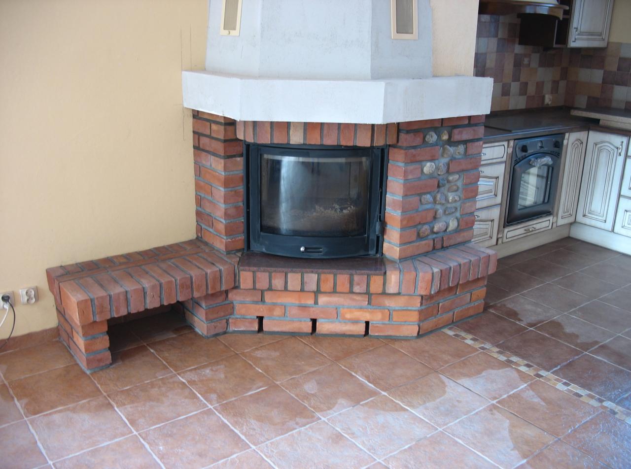 Murowany wkład kominkowy z cegły klinkierowej z siedziskiem, w tle zabudowa kuchenna.