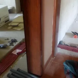 Wnętrze w trakcie remontu, widoczne czerwone rury instalacji wodnej ułożone w bruzdach w podłodze, narzędzia, kartonowe pudła i materiały budowlane porozrzucane na podłodze.