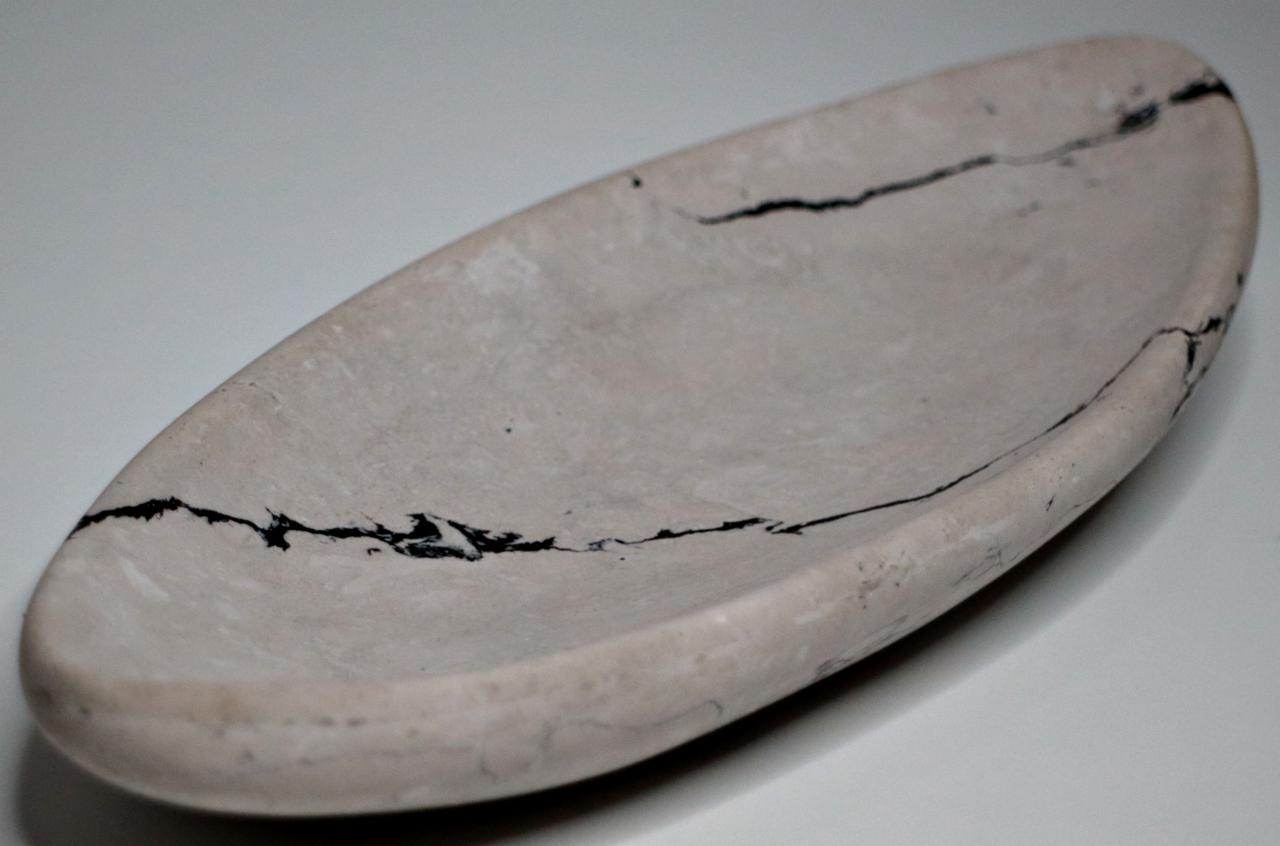 Owalna misa z jasnego kamienia z ciemnymi żyłkami, ustawiona na białym tle, ukazująca naturalny wzór kamienia.