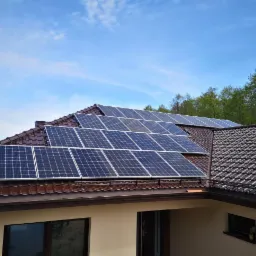 Panele słoneczne na brązowym dachu domu jednorodzinnego, błękitne niebo w tle.