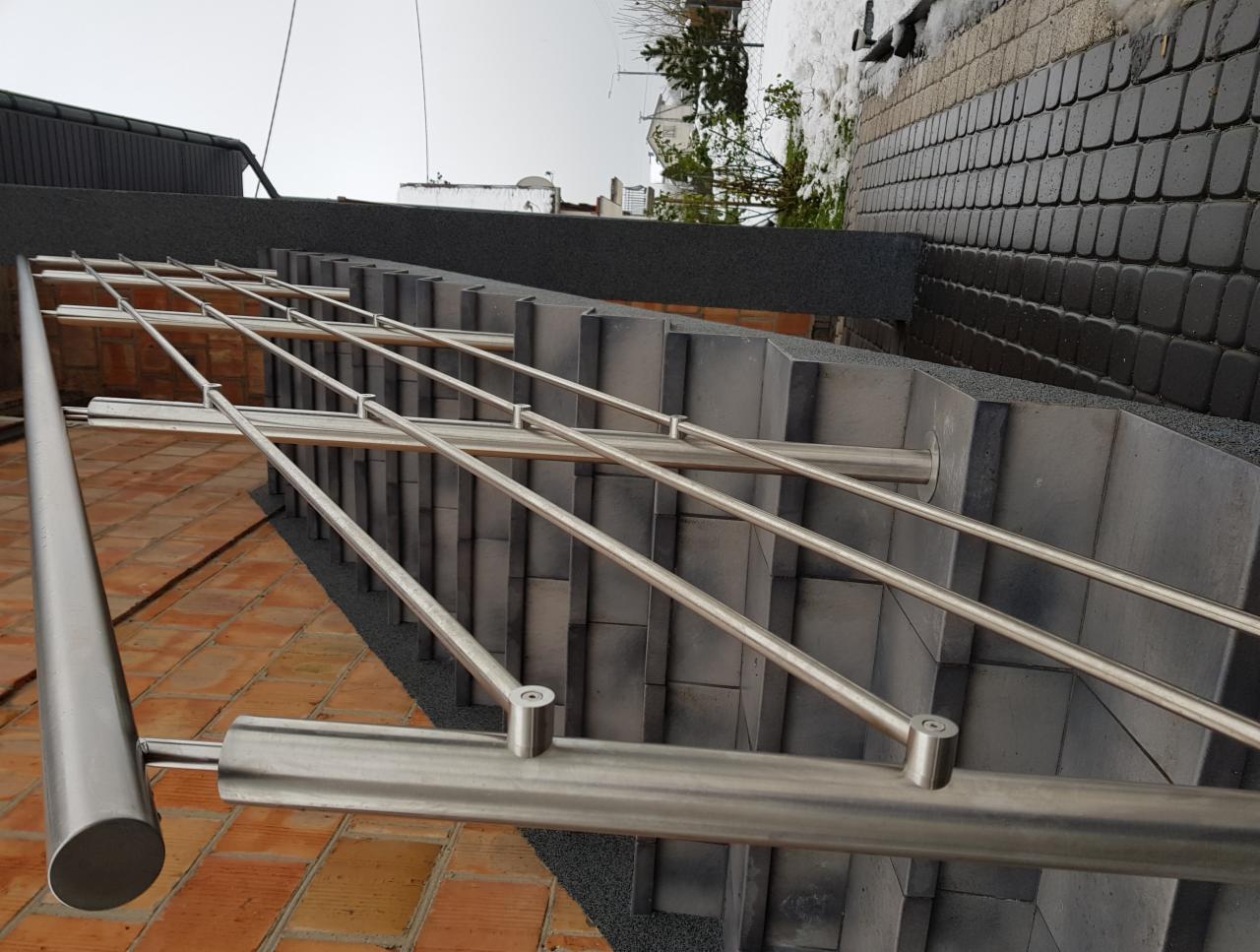 Zewnętrzne schody z szarych płyt z balustradą ze stali nierdzewnej, widok z góry pod kątem, z elementami śniegu w tle.