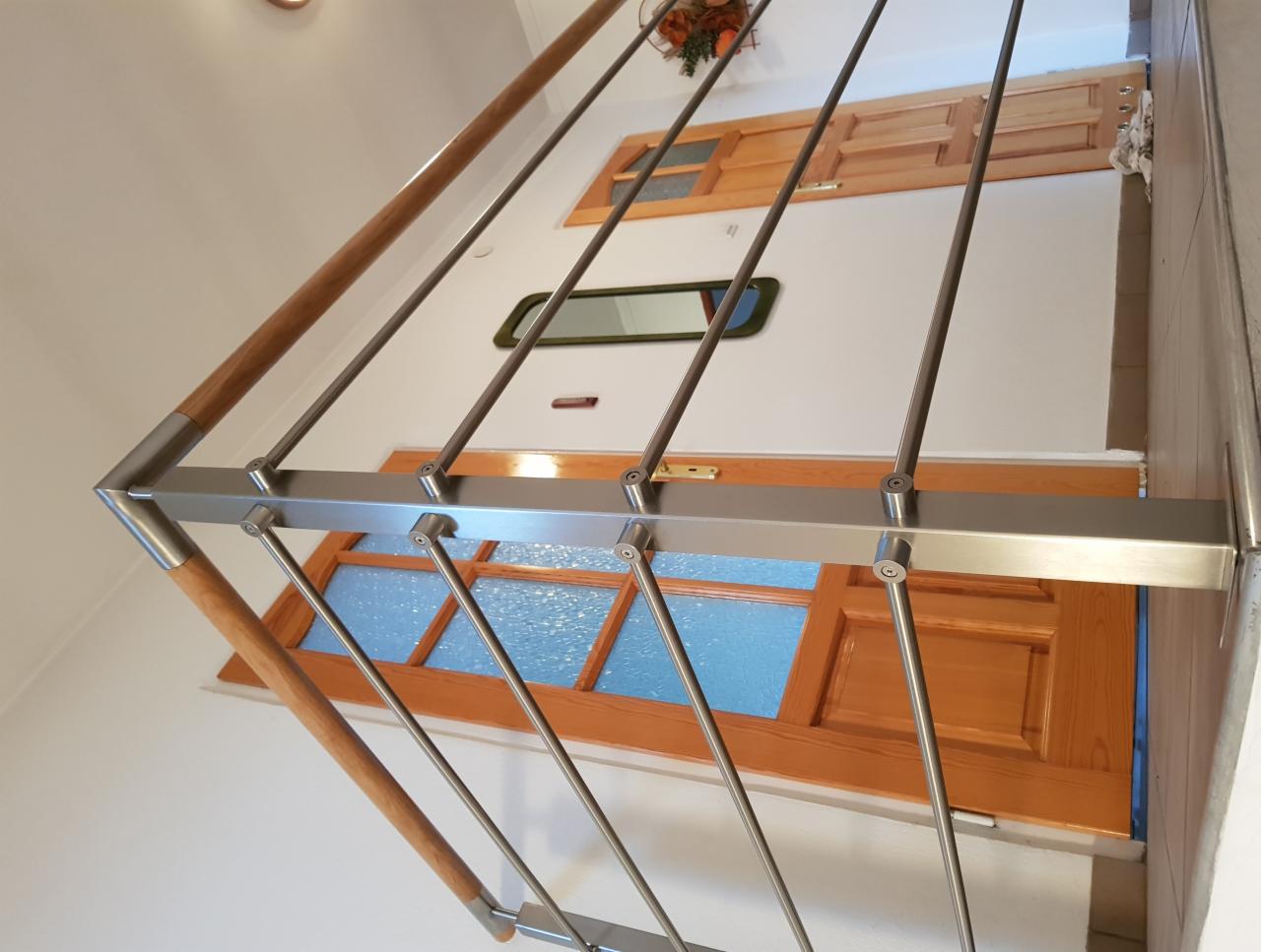 Nowoczesna balustrada ze stali nierdzewnej z drewnianymi poręczami, widok z dołu na drewniane okna i drzwi w tle.
