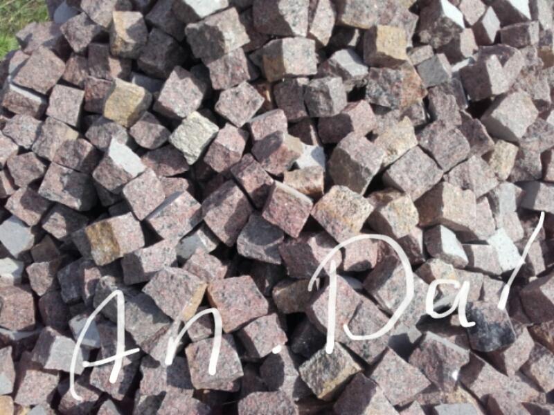 Kupa kostki granitowej w odcieniach różu i szarości, ułożona chaotycznie, z widocznym napisem 'An.Da!' nałożonym na zdjęcie.