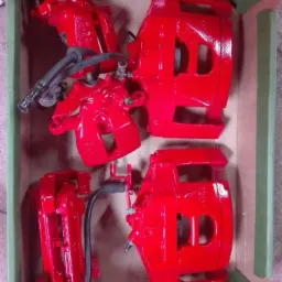 Zestaw czterech, intensywnie czerwonych zacisków hamulcowych w kartonowym pudełku, po renowacji i zabezpieczeniu powłoką.