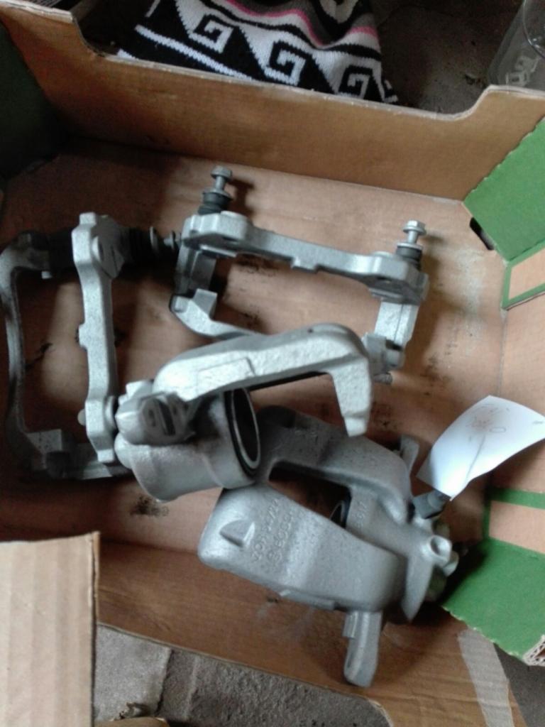 Zdemontowane, surowe zaciski hamulcowe w kartonowym pudełku, przygotowane do piaskowania lub malowania proszkowego.