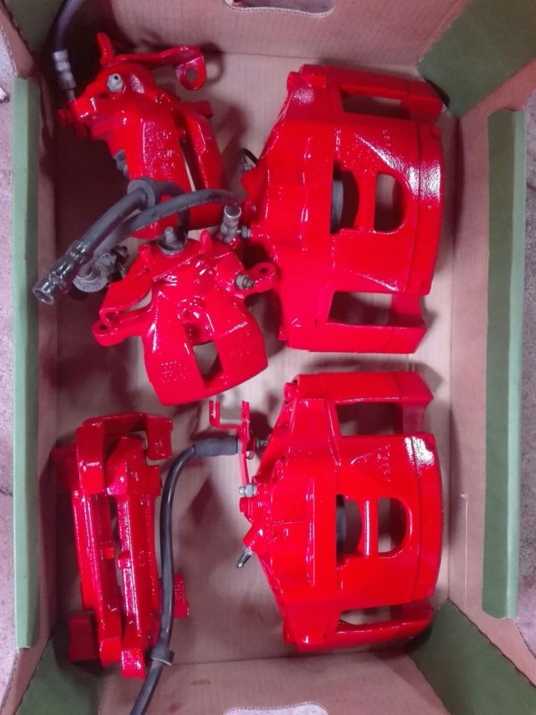 Zestaw czterech, intensywnie czerwonych zacisków hamulcowych w kartonowym pudełku, po renowacji i zabezpieczeniu powłoką.