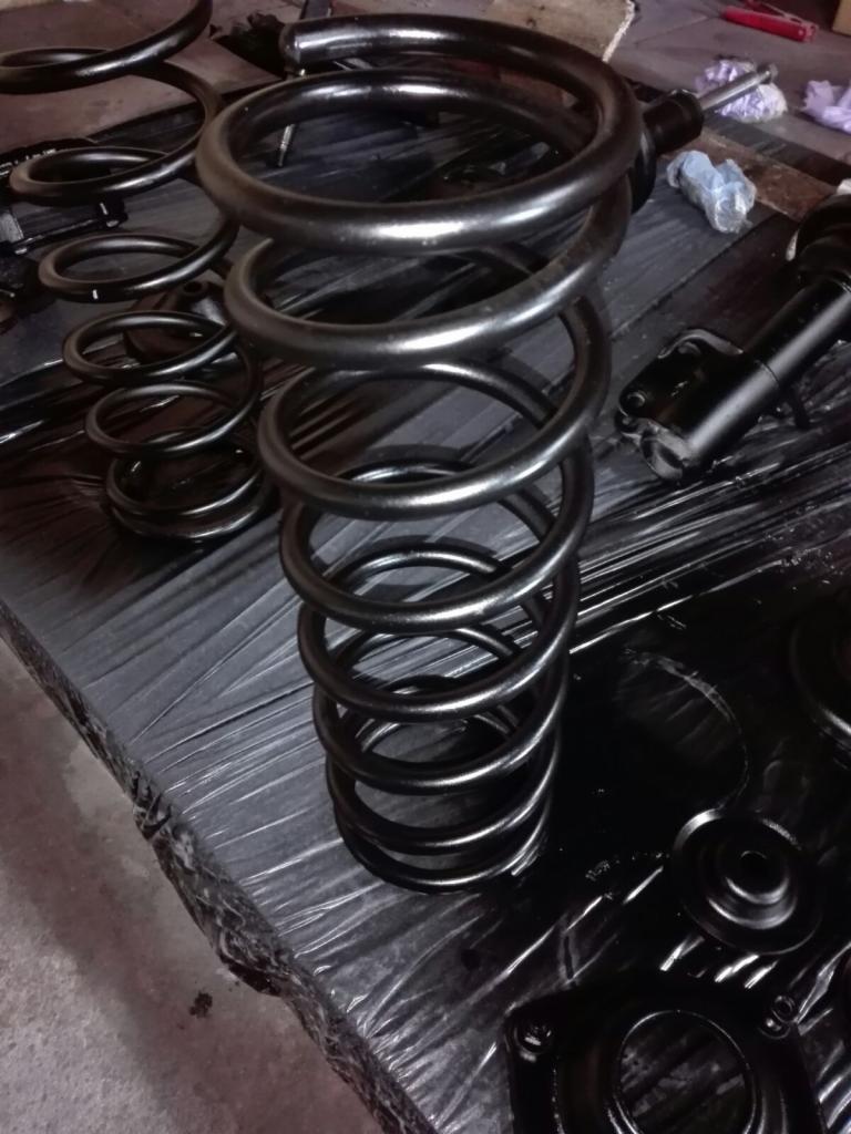 Czarne sprężyny samochodowe i elementy zawieszenia po obróbce, leżące na folii ochronnej.