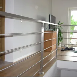 Nowoczesna, metalowa barierka schodowa z poziomymi prętami, widok z dołu, drewniana podłoga i drzwi w tle.