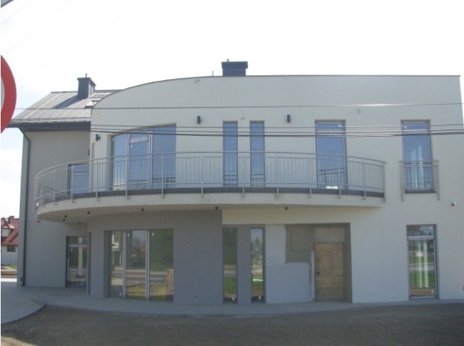 Nowoczesny dom z zaokrąglonym balkonem zabezpieczonym metalową konstrukcją, widok z zewnątrz, częściowo wykończony budynek.