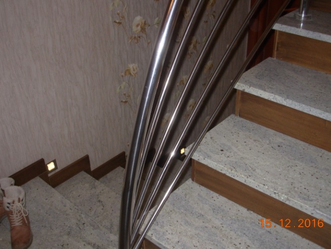 Schody z szarego granitu z drewnianymi podstopnicami i metalową, giętą balustradą z rurek, widok z góry