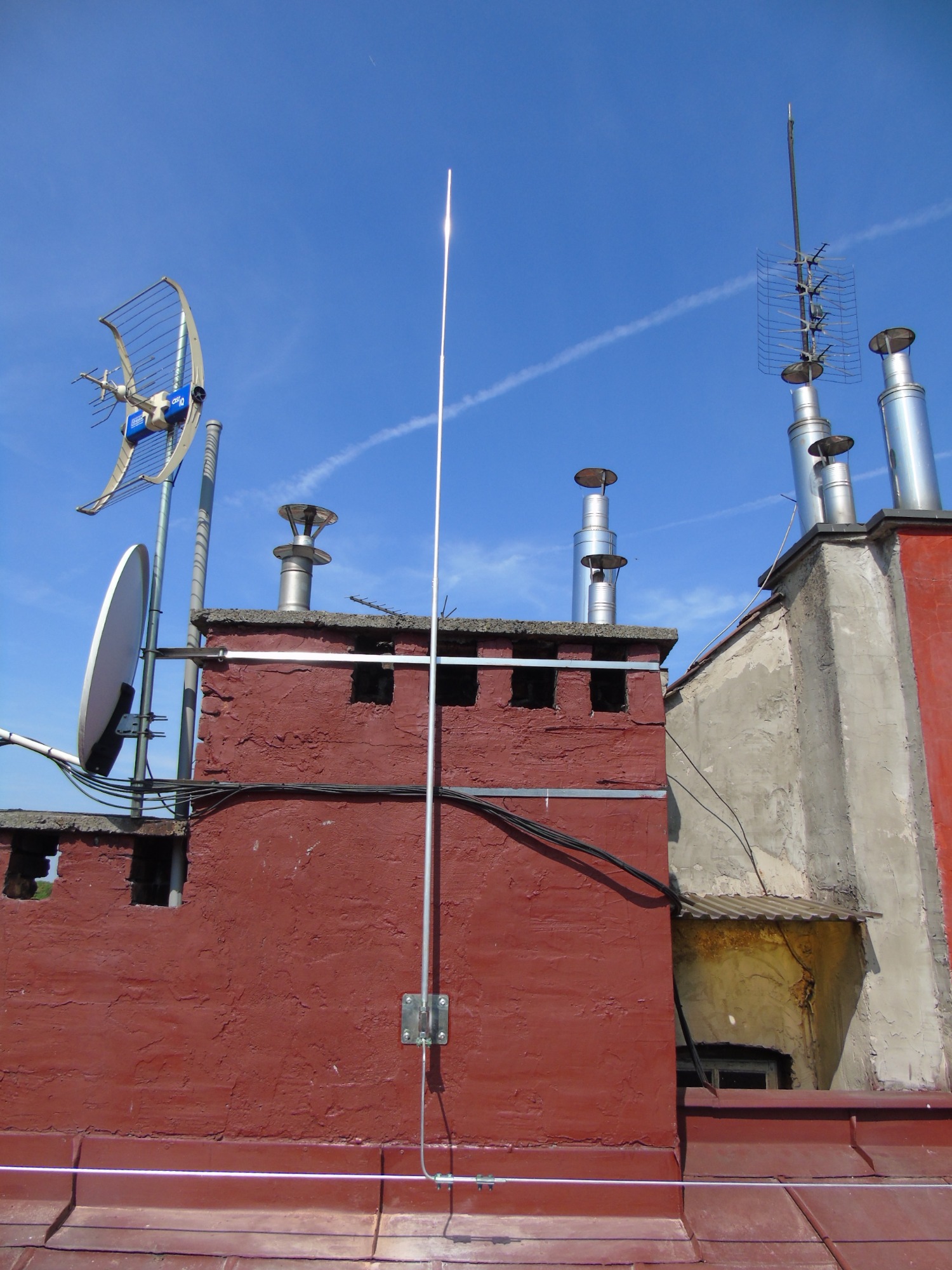 Anteny telewizyjne i satelitarne, kominy wentylacyjne i instalacja odgromowa na dachu budynku w słoneczny dzień.