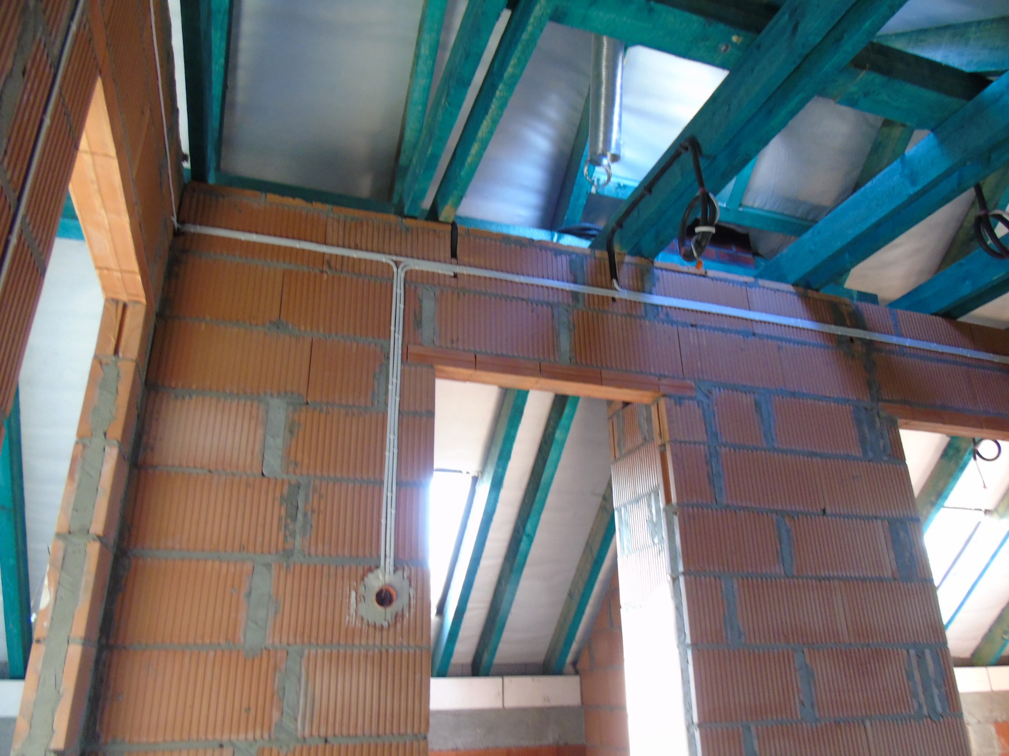 Wewnętrzne ściany z pustaków ceramicznych z rozprowadzoną instalacją elektryczną w rurkach, widoczne otwory pod gniazdka i zielone belki stropowe.