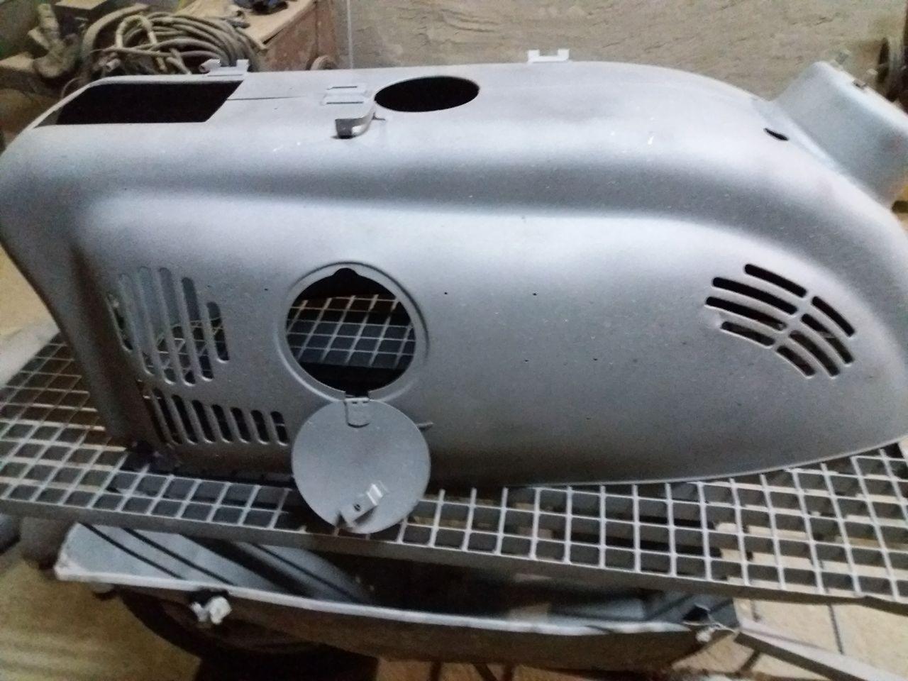 Element motocykla, prawdopodobnie zbiornik paliwa, po obróbce strumieniowo-ściernej, przygotowany do malowania, umieszczony na metalowej kratownicy.