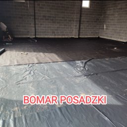 Bomar - Montaż czarnej folii na podłożu w hali w Gajówce, przygotowanie do wylewki. Widoczny pracownik w rogu pomieszczenia.
